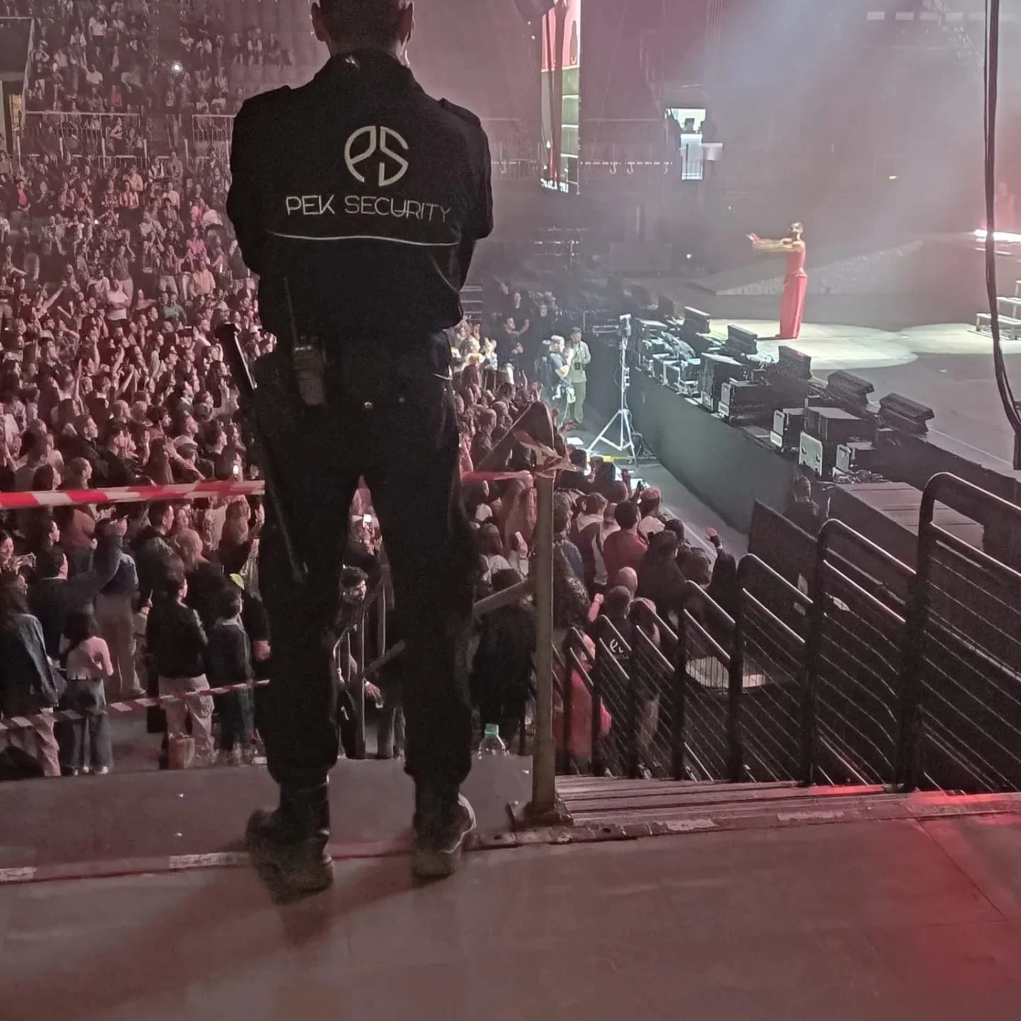 Vigilante identificado como PEK SECURITY supervisando un concierto desde una posición de vigilancia